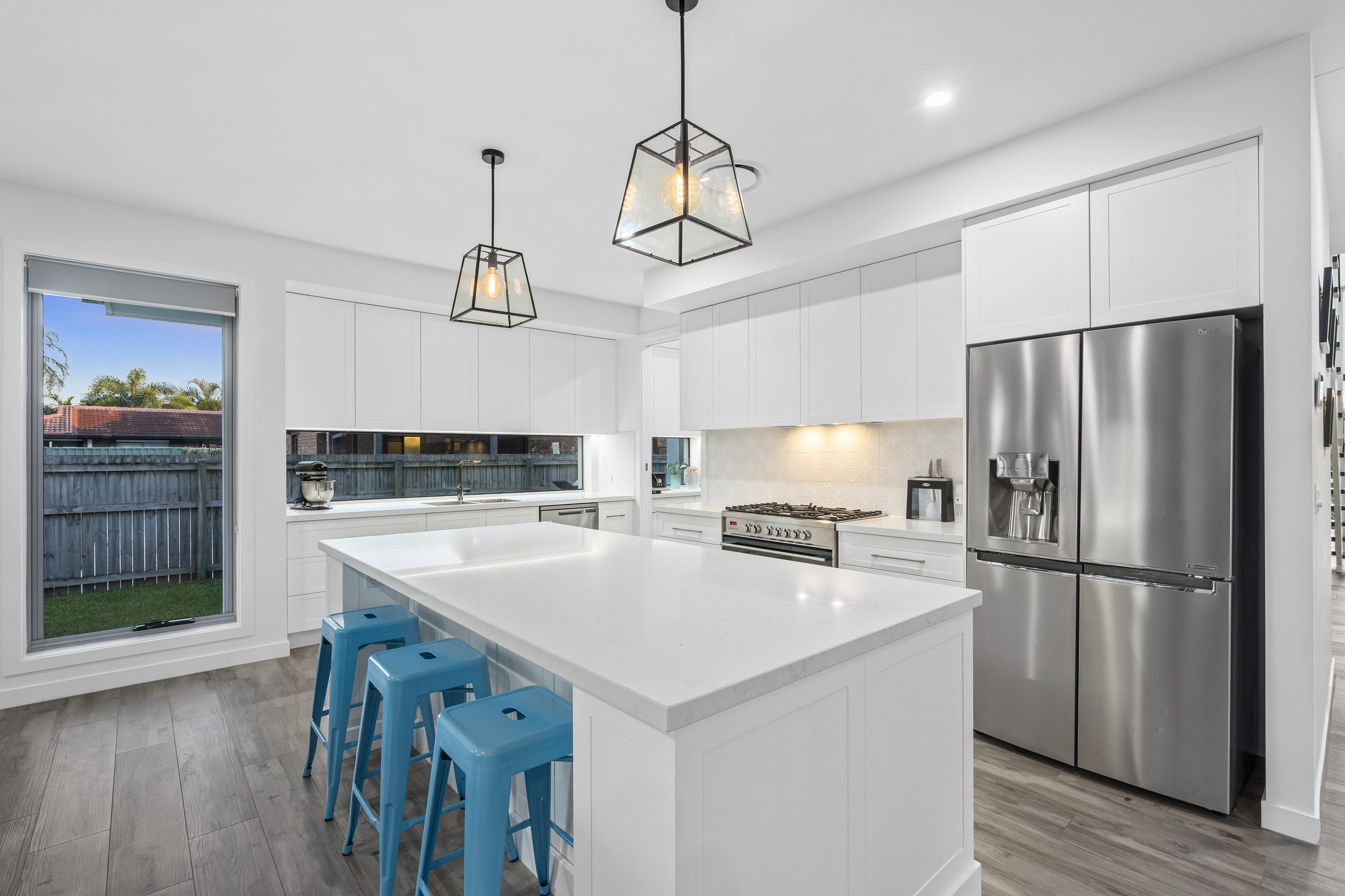 Kitchen with a stone-topped island, two pendant lights, white shaker-style joinery and a mirrored splashback.