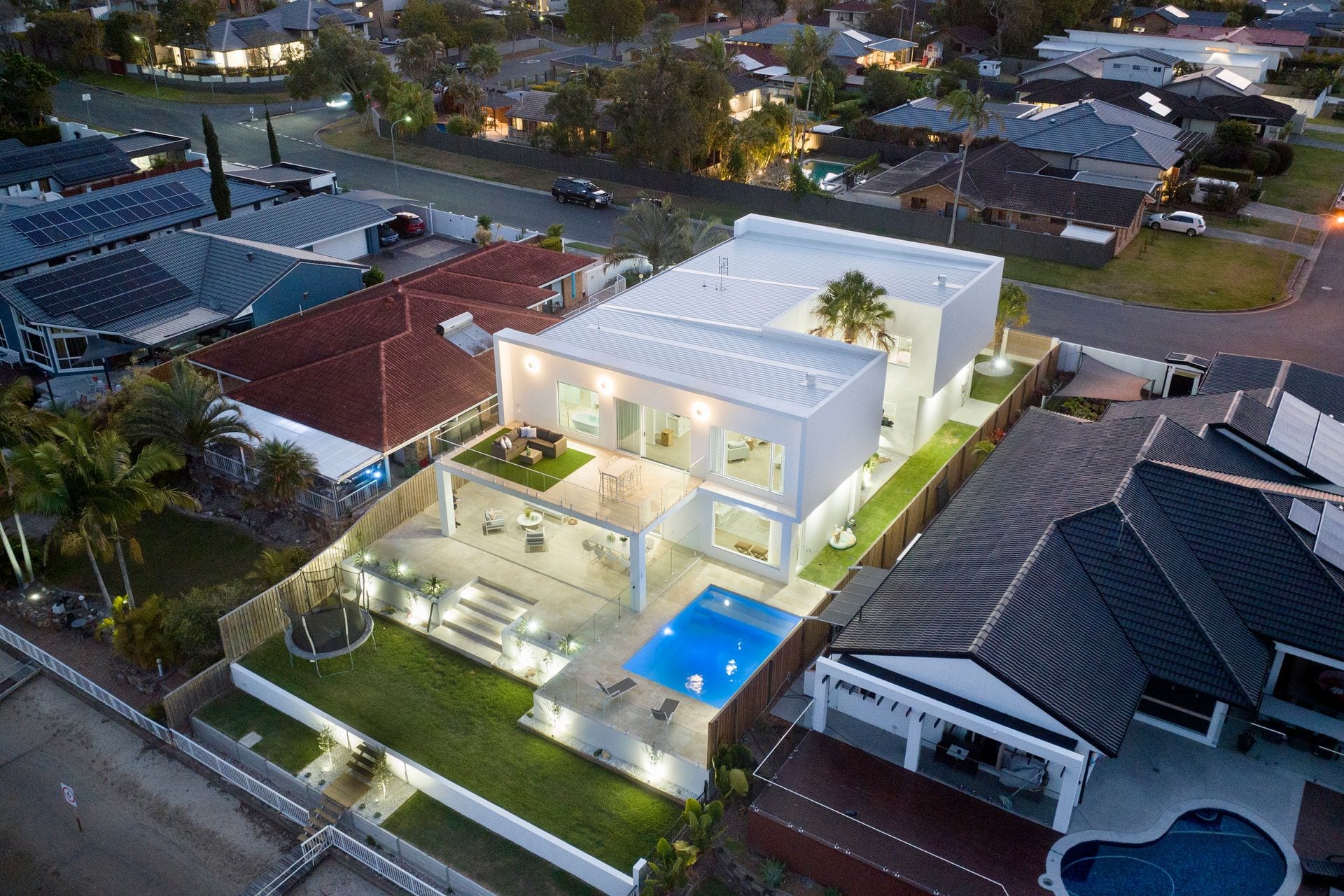 An elevated view of the house at dusk showing the flat roof forms, the covered terrace, pool and lawn arranged across the rear of the block.