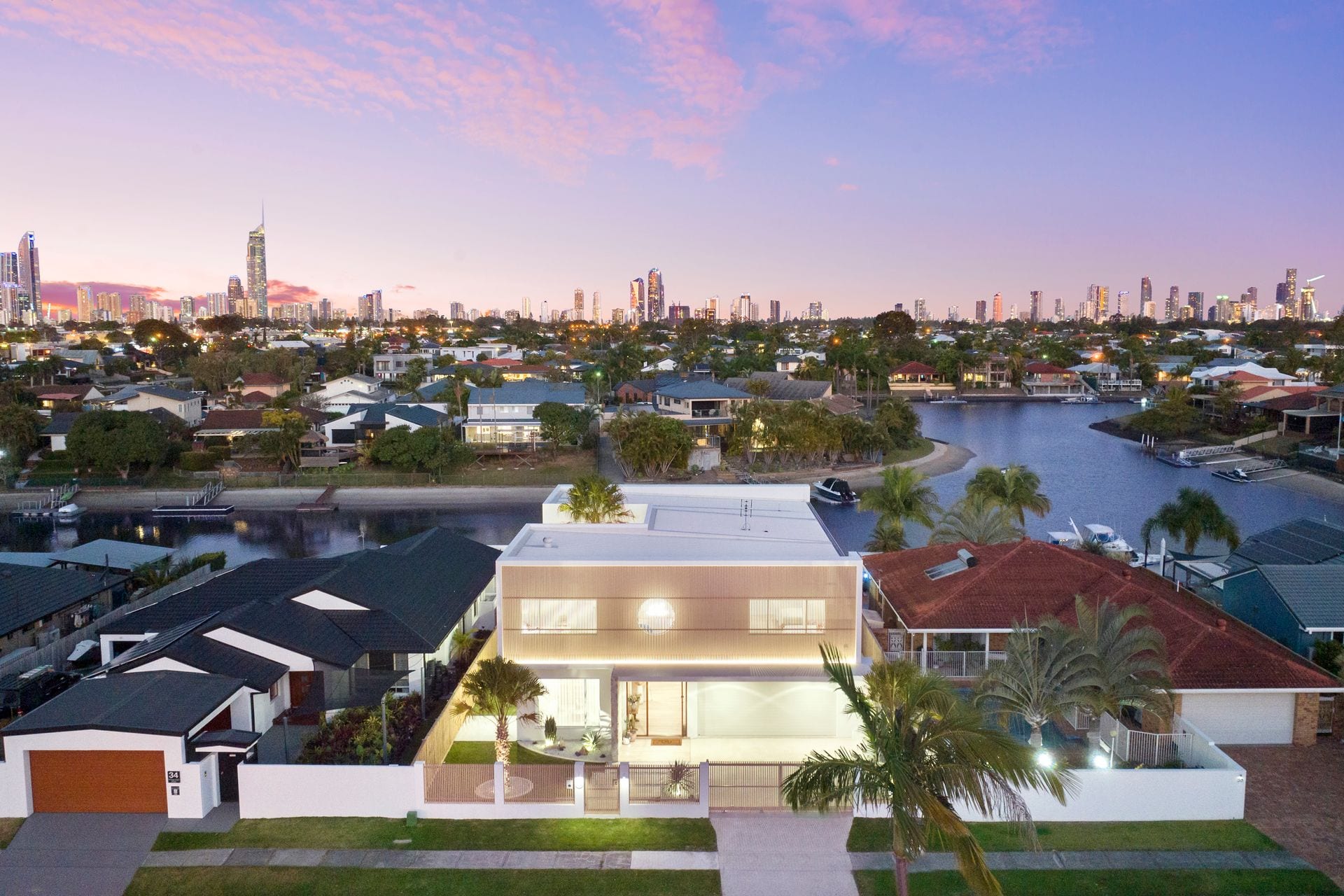 An aerial view at dusk with the residence in the foreground, the Benowa Waters canals beyond it and the Gold Coast skyline on the horizon.